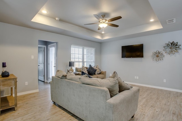 living room featuring a raised ceiling, ceiling fan, and light wood-type flooring