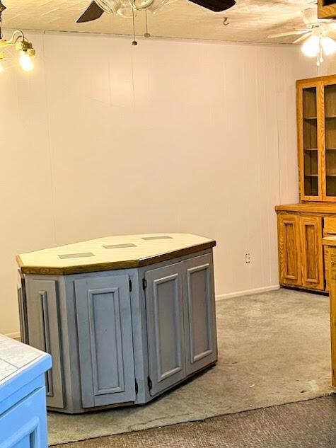 kitchen featuring ceiling fan, tile countertops, light carpet, a kitchen island, and gray cabinets