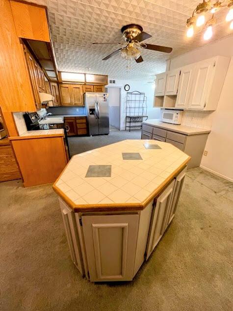 kitchen featuring tile countertops, under cabinet range hood, a kitchen island, carpet, and stainless steel fridge