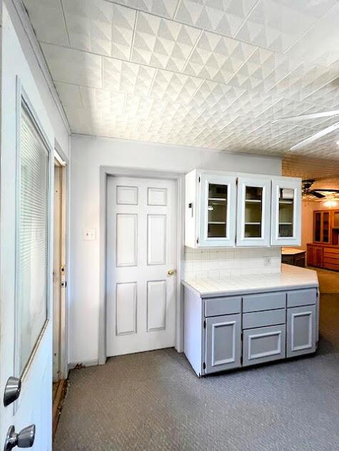 kitchen featuring ceiling fan, glass insert cabinets, gray cabinets, light countertops, and dark colored carpet