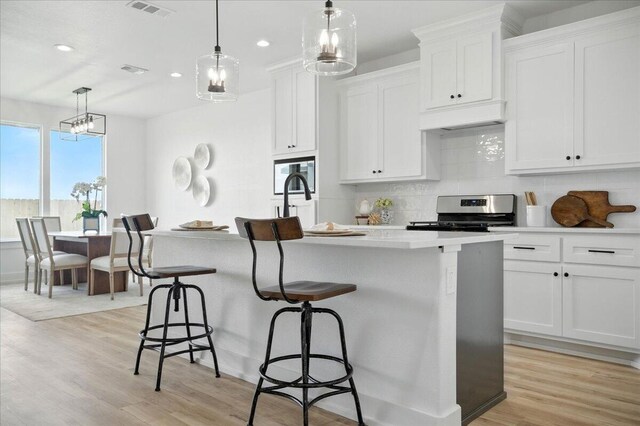 1406 Durham Ave, Wolfforth, TX 79382 - kitchen featuring stainless steel range, recessed lighting, decorative backsplash, light wood finished floors, and a center island with sink