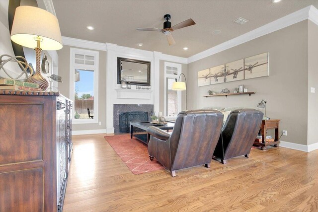 living room with a tiled fireplace, ornamental molding, ceiling fan, and light hardwood / wood-style flooring