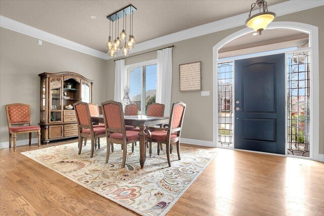 dining space with ornamental molding, a chandelier, a textured ceiling, and light hardwood / wood-style floors