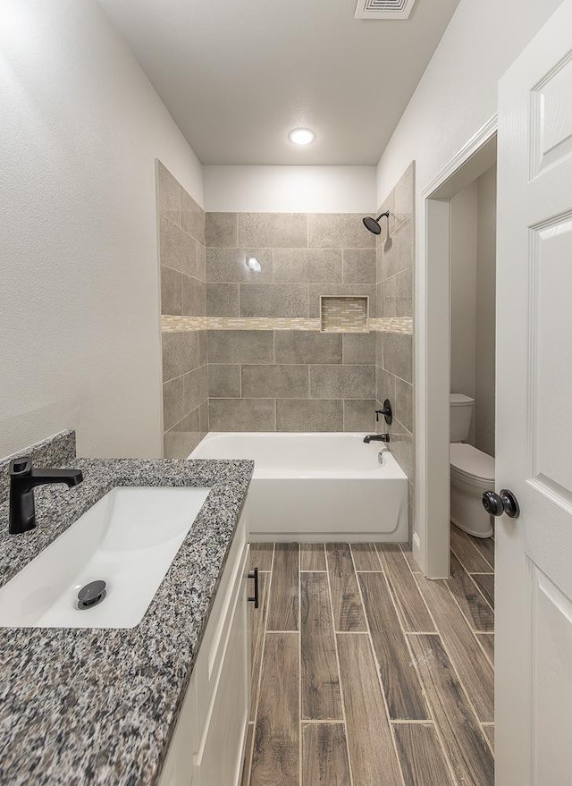 full bathroom with vanity, tiled shower / bath, and toilet