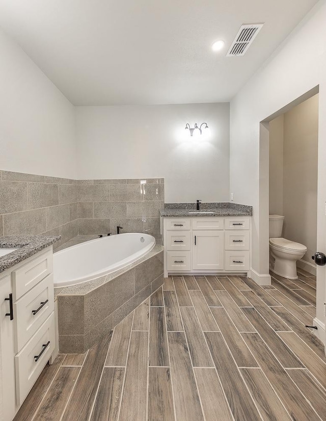 bathroom featuring vanity, tiled bath, and toilet