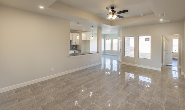 unfurnished living room featuring ceiling fan with notable chandelier and a raised ceiling