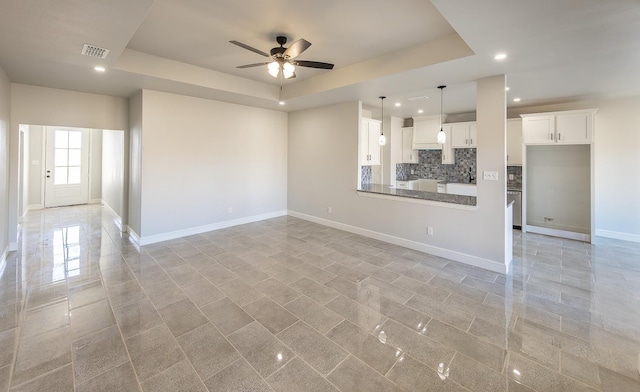 unfurnished living room featuring ceiling fan and a raised ceiling