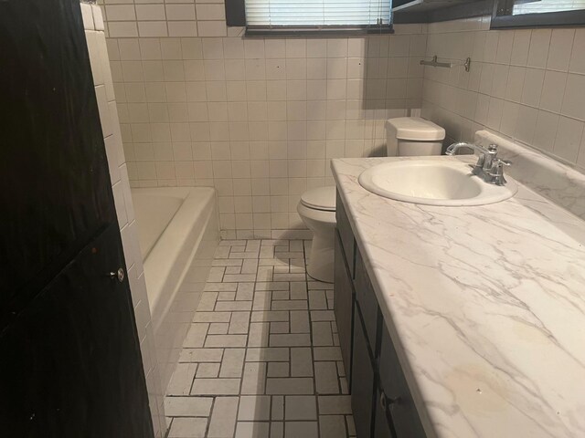 bathroom featuring a tub to relax in, vanity, toilet, and tile walls