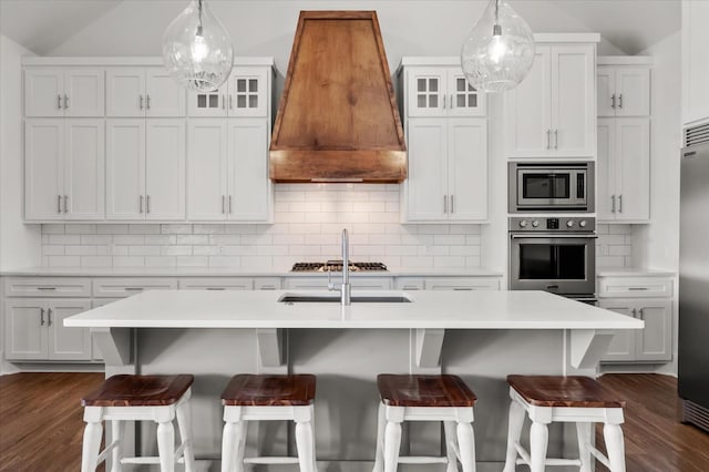 kitchen featuring white cabinetry, custom range hood, built in appliances, and an island with sink