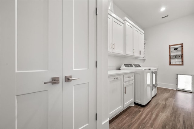 clothes washing area with cabinets, washing machine and dryer, and dark wood-type flooring