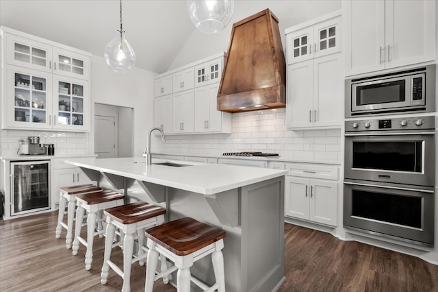 kitchen with sink, appliances with stainless steel finishes, wine cooler, white cabinets, and custom exhaust hood