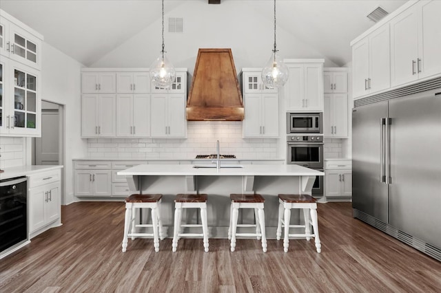 kitchen with built in appliances, white cabinetry, a kitchen island with sink, and premium range hood