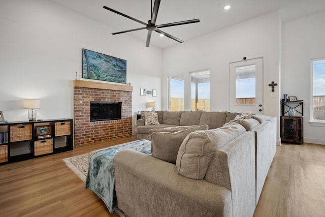 living room with a brick fireplace, ceiling fan, and light hardwood / wood-style flooring