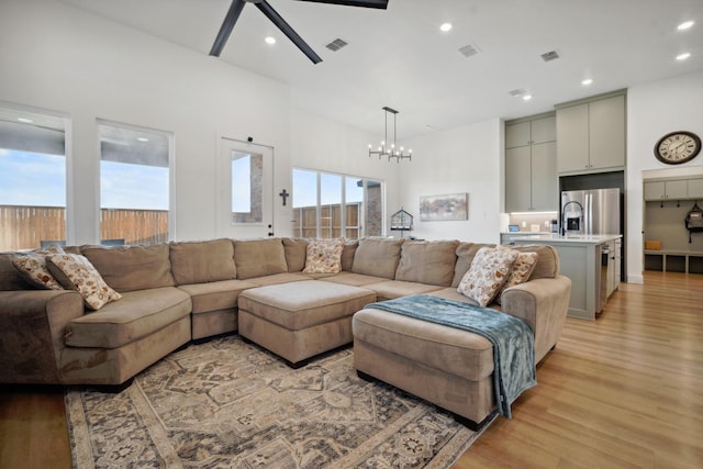 living room with ceiling fan with notable chandelier, light hardwood / wood-style flooring, and a high ceiling