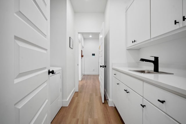 corridor with washer / clothes dryer, sink, and light hardwood / wood-style flooring