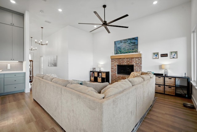 living room featuring light wood-type flooring, ceiling fan with notable chandelier, and a fireplace