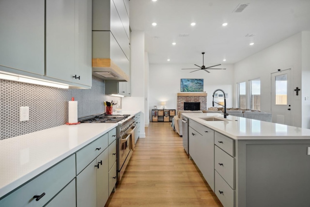 kitchen with sink, appliances with stainless steel finishes, an island with sink, a brick fireplace, and light wood-type flooring