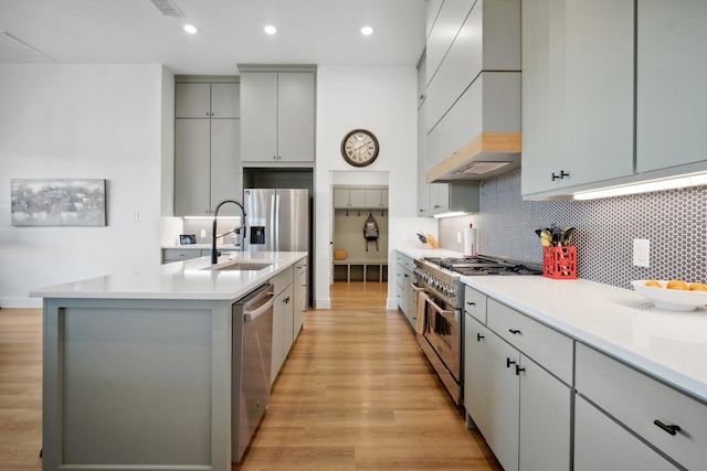 kitchen with premium range hood, sink, a center island with sink, light hardwood / wood-style flooring, and stainless steel appliances