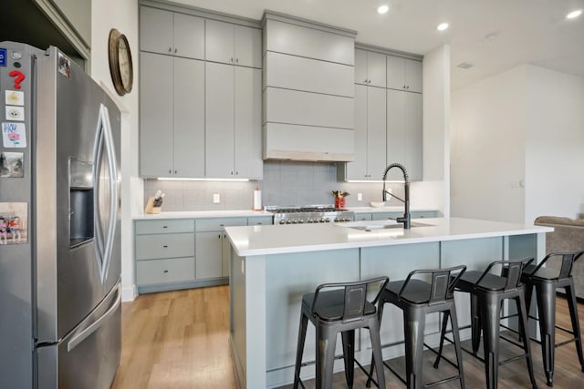 kitchen featuring sink, a breakfast bar area, an island with sink, stainless steel fridge with ice dispenser, and light wood-type flooring