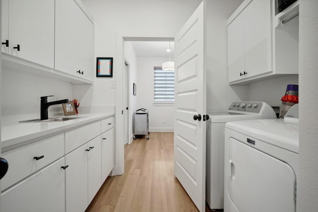 laundry area with cabinets, separate washer and dryer, sink, and light hardwood / wood-style flooring