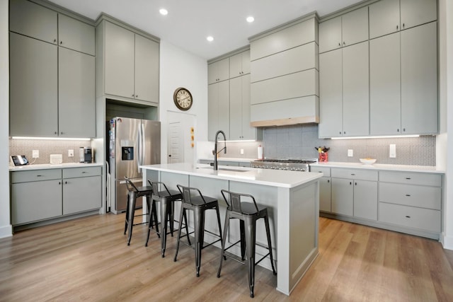 kitchen featuring gray cabinets, sink, a kitchen bar, stainless steel fridge with ice dispenser, and a center island with sink