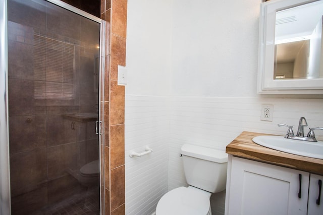 bathroom featuring a shower with door, vanity, tile walls, and toilet