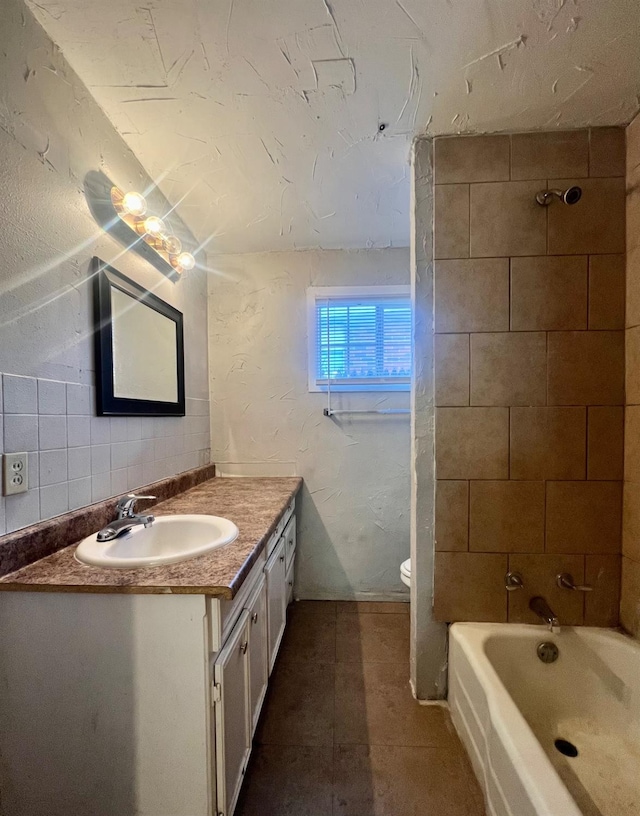 full bathroom with tile patterned flooring, backsplash, vanity, tiled shower / bath, and toilet