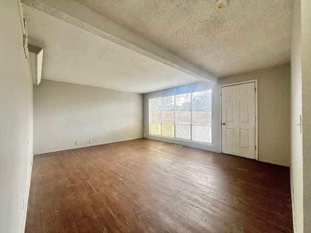 unfurnished room with dark wood-type flooring, beam ceiling, and a textured ceiling