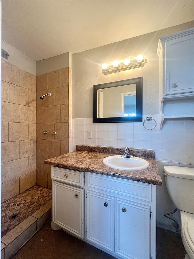 bathroom with vanity, toilet, tile walls, and a tile shower