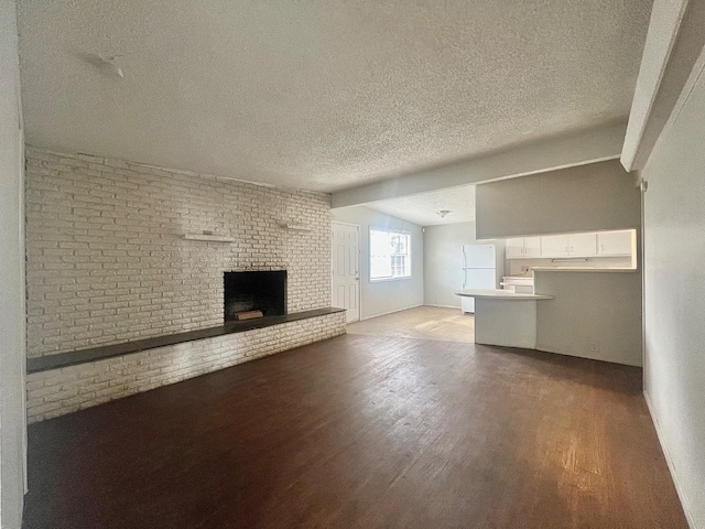 unfurnished living room with hardwood / wood-style flooring, vaulted ceiling with beams, a textured ceiling, brick wall, and a brick fireplace