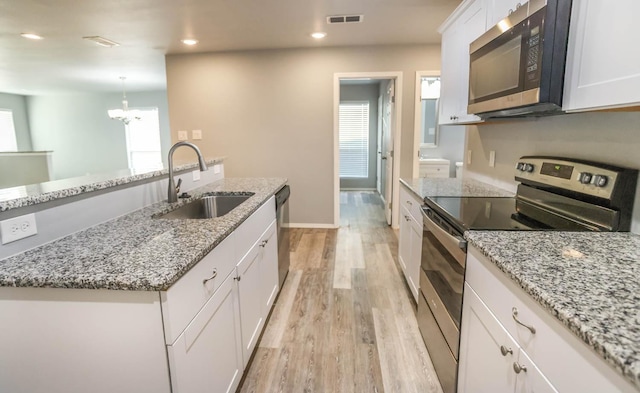 kitchen with appliances with stainless steel finishes, sink, white cabinets, and light wood-type flooring