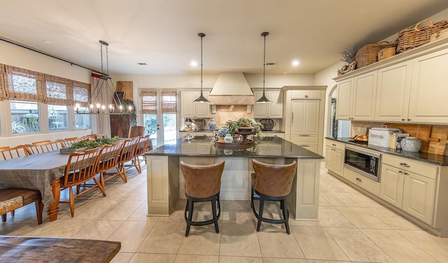 kitchen featuring premium range hood, a kitchen island, black microwave, backsplash, and hanging light fixtures