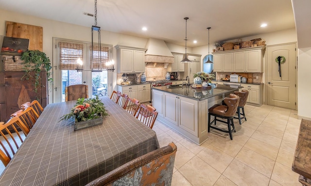 kitchen featuring pendant lighting, a breakfast bar, a kitchen island with sink, backsplash, and custom range hood