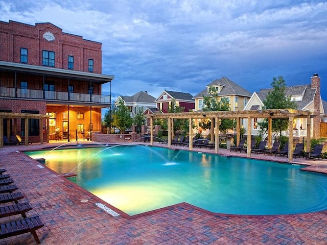 pool at dusk with pool water feature, a patio area, and a pergola