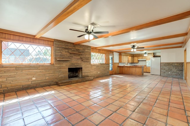 unfurnished living room with beamed ceiling, ceiling fan, a stone fireplace, and light tile patterned floors