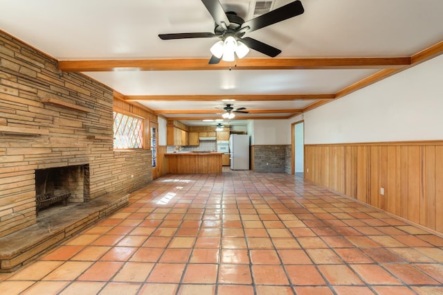 unfurnished living room featuring a stone fireplace, light tile patterned floors, wooden walls, beamed ceiling, and ceiling fan