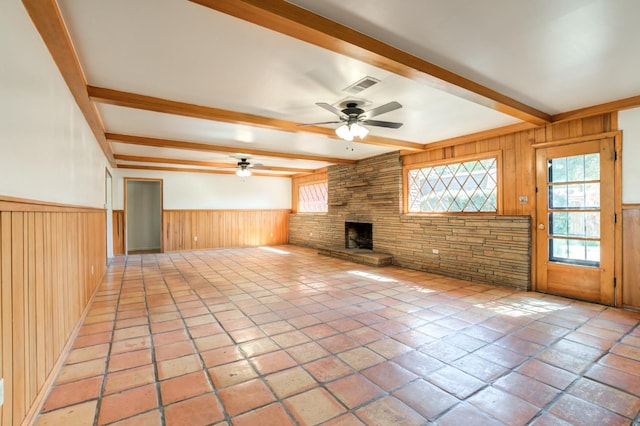 unfurnished living room featuring beam ceiling, a fireplace, ceiling fan, and wood walls