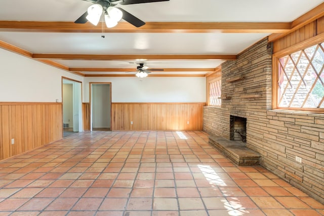 unfurnished living room with light tile patterned floors, ceiling fan, beam ceiling, wooden walls, and a fireplace