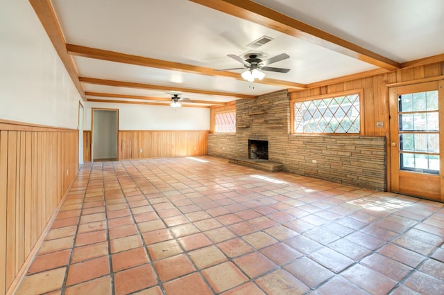 unfurnished living room with ceiling fan, wooden walls, a fireplace, and beam ceiling