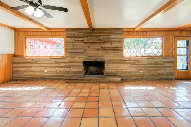 unfurnished living room with wooden walls, tile patterned floors, a stone fireplace, and beam ceiling