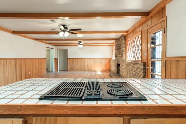 kitchen featuring beamed ceiling, black electric stovetop, tile countertops, and wooden walls