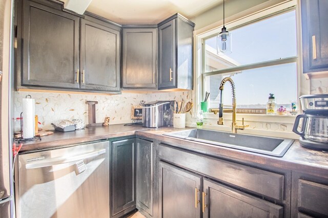 kitchen with stainless steel dishwasher, sink, hanging light fixtures, and backsplash