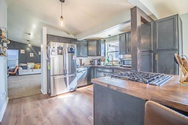 kitchen with butcher block countertops, sink, appliances with stainless steel finishes, hanging light fixtures, and vaulted ceiling