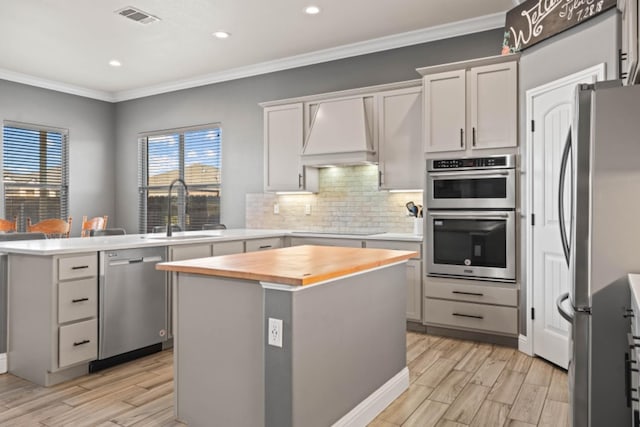 kitchen featuring sink, premium range hood, stainless steel appliances, a kitchen island, and wood counters