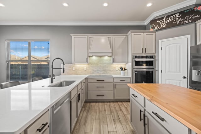 kitchen with sink, custom exhaust hood, stainless steel appliances, and wooden counters