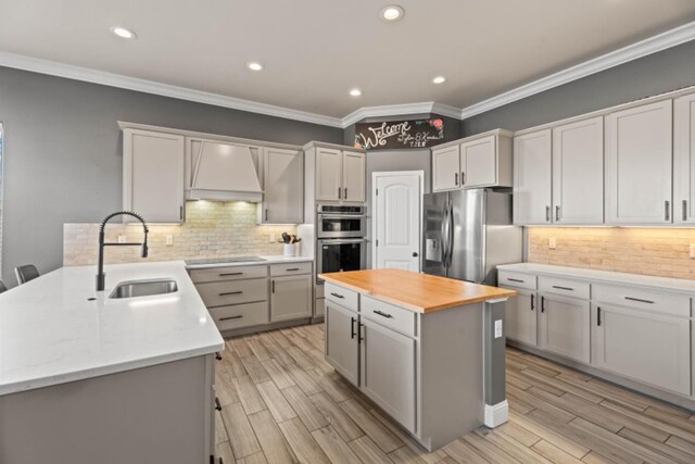 kitchen with butcher block countertops, sink, stainless steel appliances, a center island, and custom range hood