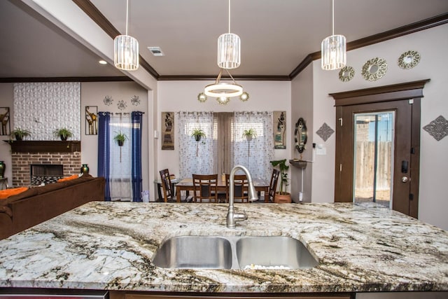 kitchen with light stone counters, crown molding, sink, and hanging light fixtures