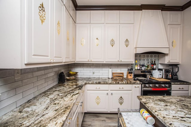 kitchen featuring tasteful backsplash, white cabinetry, custom exhaust hood, stainless steel gas range oven, and light stone countertops