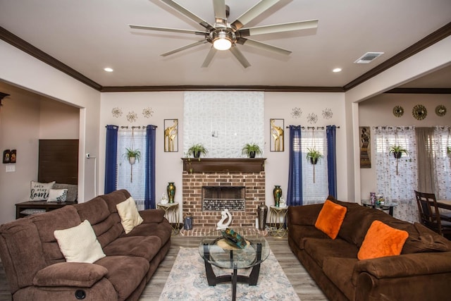 living room with a brick fireplace, ornamental molding, light hardwood / wood-style floors, and ceiling fan