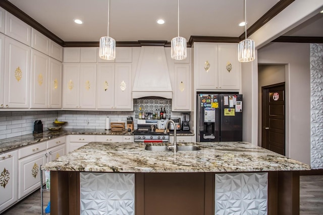 kitchen featuring premium range hood, black fridge with ice dispenser, hanging light fixtures, a large island with sink, and light stone countertops